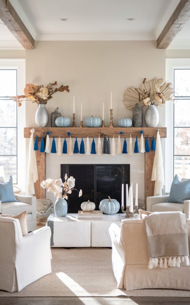 A photo of a posh farmhouse-style living room with a beautifully decorated mantel as the focal point. The mantel is adorned with blue and white tassels, white candles, blue ceramic pumpkins, and small vases with dried florals. The room features elegant farmhouse elements such as neutral-toned furniture, soft textiles, wooden beams, and metallic accents. Natural light filters in through large windows, casting a warm glow on the room.