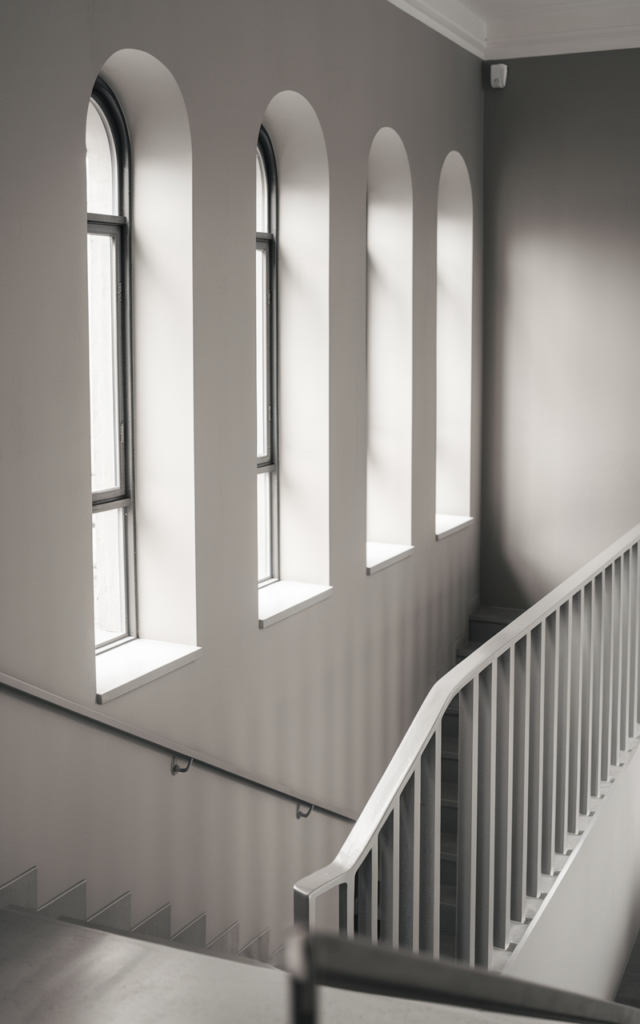 An elegant and natural-looking realistic photograph of a staircase featuring a minimalist monochrome window wall with frames matching the wall color, sleek railings and clean lines creating a serene atmosphere decorated in minimalist style with natural lighting