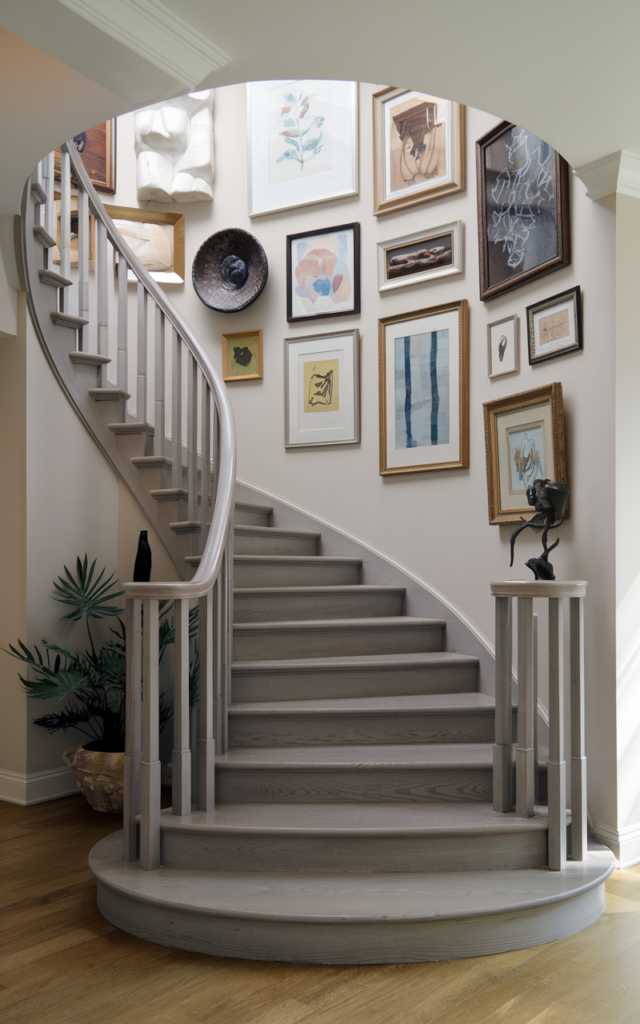 An elegant and natural-looking realistic photograph of a circular staircase with a curated gallery wall of framed artwork following the spiral wall upward in a stylish home interior decorated in contemporary gallery-style interior design with natural lighting