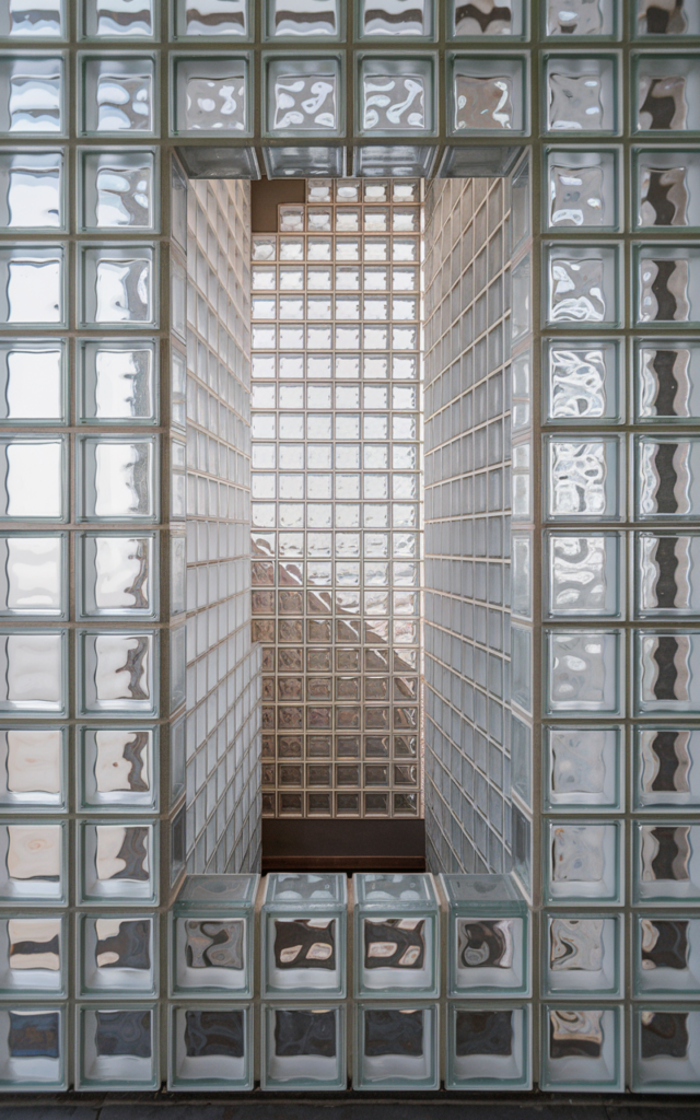 An elegant and natural-looking realistic photograph of a staircase enclosure framed with clear glass blocks arranged in a clean grid allowing diffused light to pass through decorated in modern retro-inspired style with natural lighting