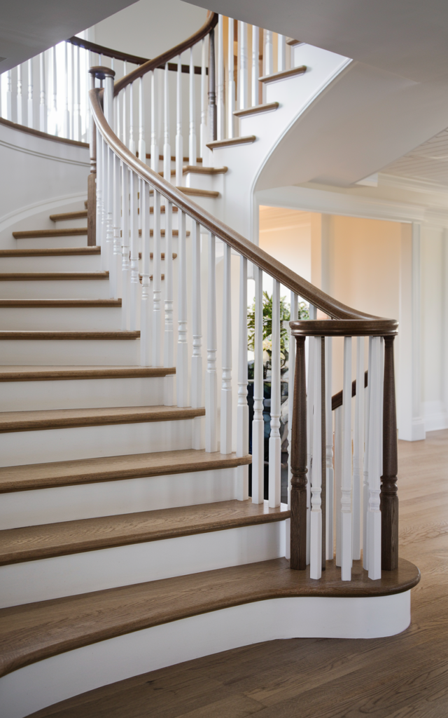 An elegant and natural-looking realistic photograph of a staircase with white balusters and a contrasting deep walnut handrail creating bold visual contrast beside light oak stairs decorated in classic transitional home decor style with natural lighting