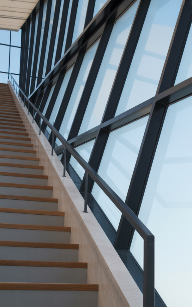 An elegant and natural-looking realistic photograph of a custom staircase with a window wall that follows the exact angle of the stair incline, featuring expansive glazing and sleek handrails decorated in contemporary architectural style with natural lighting