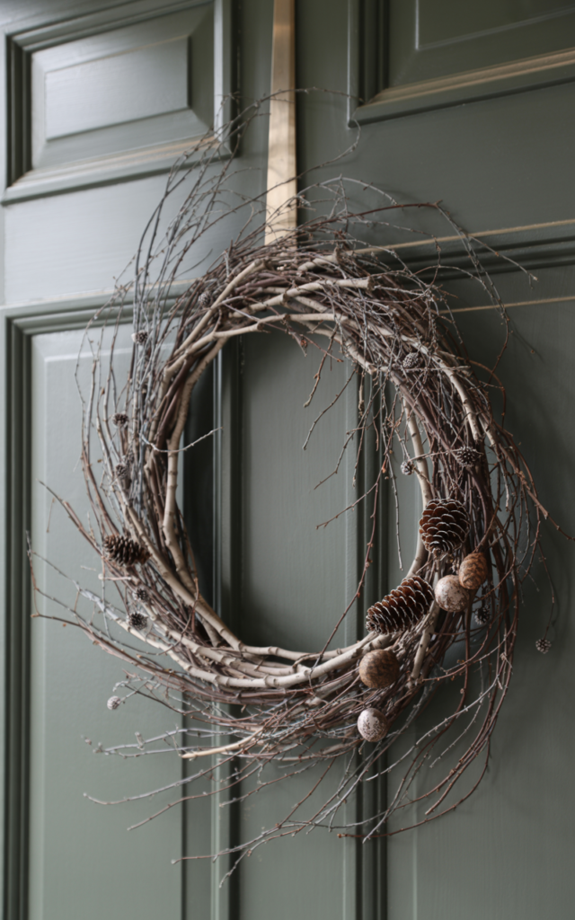 An elegant and natural-looking realistic photograph of a winter front door featuring a wreath made from bare twigs and branches with minimal accents creating a raw natural look decorated in organic minimalist style with natural lighting