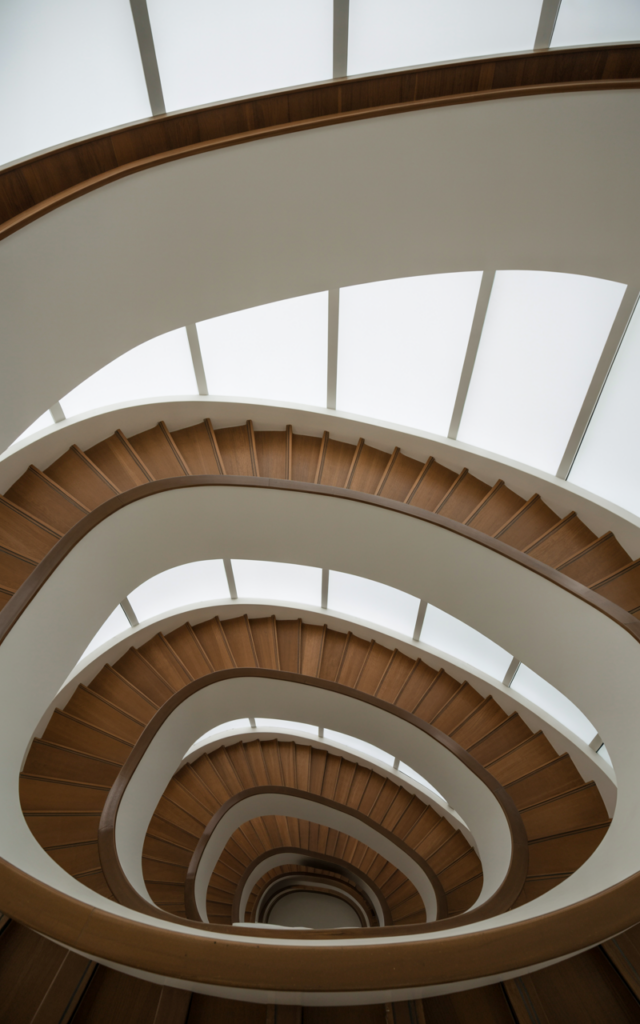 An elegant and natural-looking realistic photograph of a tall multi-floor staircase with a continuous wooden handrail flowing seamlessly across multiple levels along a clean wall beside modern stair flights decorated in modern architectural home decor style with natural lighting