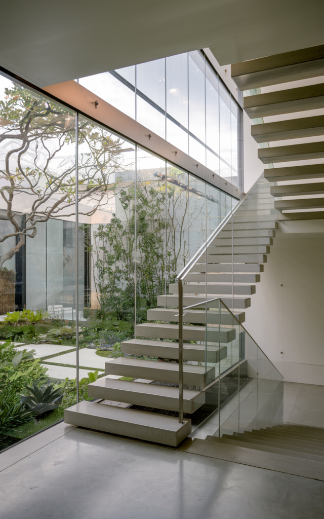 An elegant and natural-looking realistic photograph of a staircase with frameless glass windows providing uninterrupted garden views, paired with sleek floating stairs and minimalist railing decorated in ultra-modern style with natural lighting