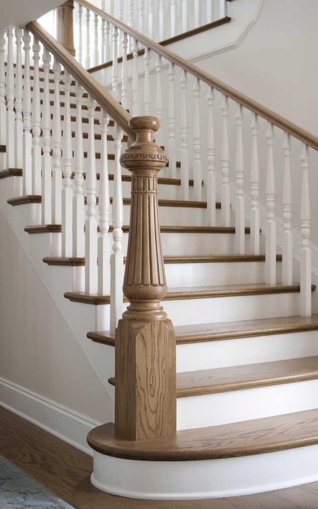 An elegant and natural-looking realistic photograph of a staircase featuring a sculptural turned wood newel post at the base, classic white balusters and medium tone wood treads decorated in refined traditional style with natural lighting