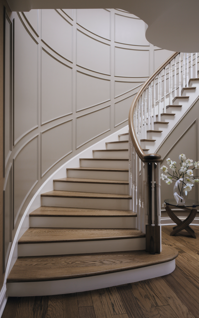 An elegant and natural-looking realistic photograph of a curved staircase wall with flexible curved molding panels following the graceful flow of the staircase beside elegant curved wooden steps and railing decorated in luxury contemporary home decor style with natural lighting