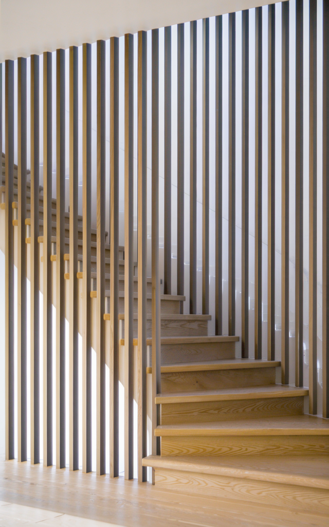An elegant and natural-looking realistic photograph of a staircase enclosed with vertical natural oak wood slats providing partial privacy and architectural detail decorated in Scandinavian modern style with natural lighting